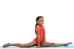 Young gymnast doing a split on a blue mat.